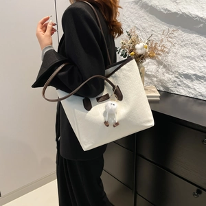 Cream tote bag with brown trim and plush charm shown on model in modern home setting