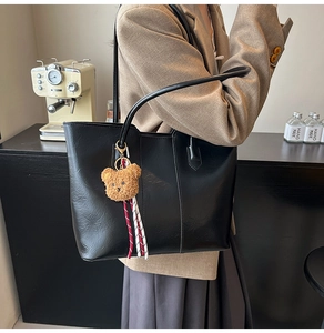 Detail of a large black tote bag with brown bear charm and rope detail in a street scene