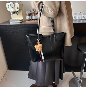 Close-up of black leather tote bag with a brown plush bear charm in a cafe setting