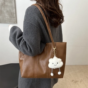 Brown leather tote bag with cloud pendant shown on shoulder for daily fashion style