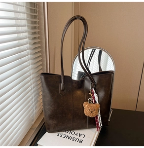 Detail of deep brown tote bag with vintage glossy leather and cute plush bear accessory