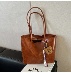 Detail of caramel tote bag with plush bear charm on a sofa in a modern home setting