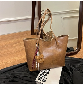 Detail of a brown faux leather tote bag with teddy bear charm on a mirror surface