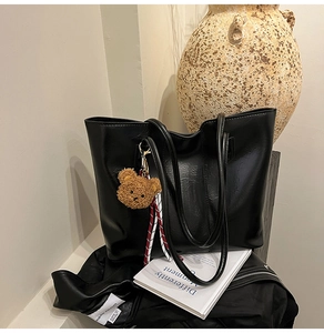 Close-up of black glossy PU leather tote bag with a cute brown plush bear charm