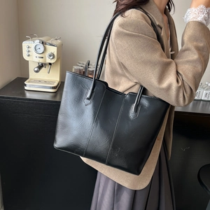 Minimalist black leather tote bag for women showing a stylish shoulder carry pose in a cafe