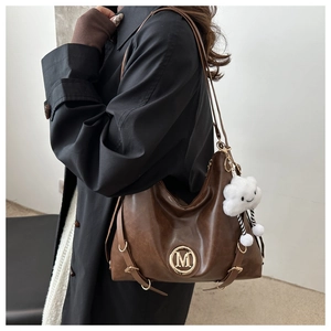 Detail of vintage dark brown tote bag with gold M logo and white cloud plush charm