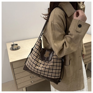 Detail of a brown plaid tote bag with a cute plush bear patch and leather straps