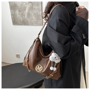 Close-up of retro brown leather tote bag with gold M logo and cloud plush charm
