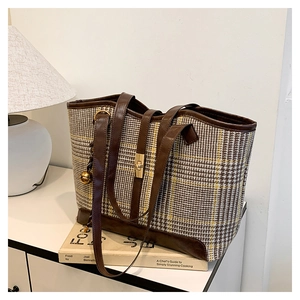 Détail du sac cabas en pied-de-poule avec bordure en cuir marron et breloque cloche dorée