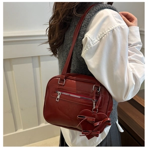 Detalle del bolso de charol rojo oscuro con cremalleras y colgante de corazón