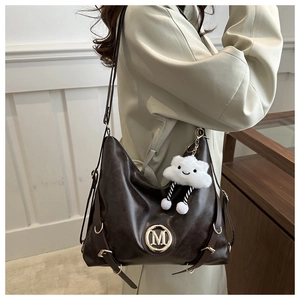 Detail of dark brown leather hobo bag with M-logo and cloud plush charm on green suit