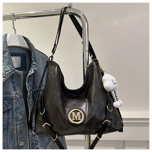 Detail of black Hobo bag featuring a gold M logo and a white cloud plush charm
