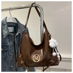 Detail view of dark brown pebbled leather tote bag with gold M logo and cloud plush charm