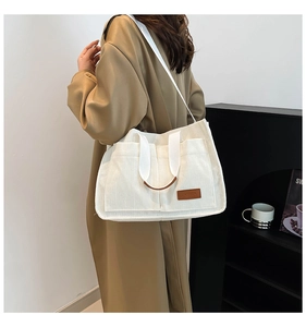 Detailed macro view of white corduroy tote bag with multiple pockets and fashion label
