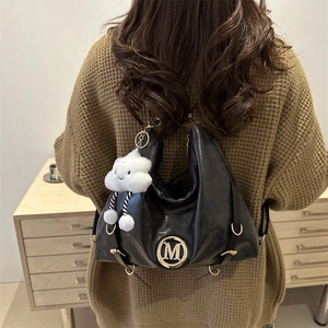 Fashionable black leather crescent tote bag with gold M logo and white plush pendant
