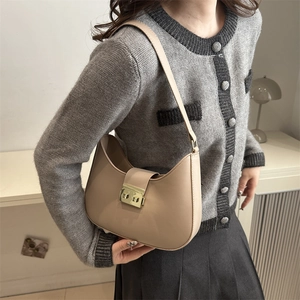 Chic beige crescent shoulder bag with golden metallic lock shown on model indoors