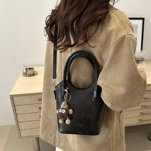 Elegant black synthetic leather bucket bag with plush charm and adjustable strap