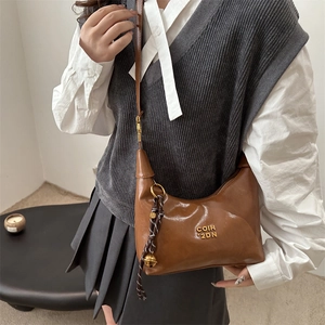 Sac demi-lune marron en similicuir avec logo doré et pendentif tressé sur modèle