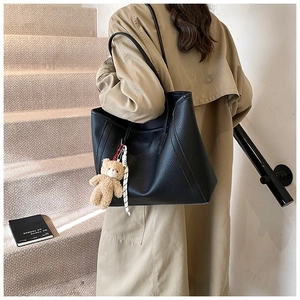 Détail du sac cabas en cuir grainé noir avec un charm ours en peluche sur un manteau