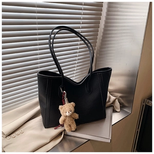 Détail d'un sac cabas en cuir grainé noir avec fines bandoulières et charm ours en peluche