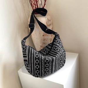 Geometric woven tote bag with adjustable strap on white pedestal in minimalist setting