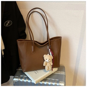 Détail d'un grand cabas en cuir marron grainé avec pendentif ours sur une valise
