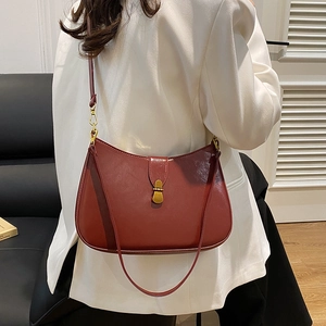 Minimalist burgundy crescent underarm bag with gold buckle on a model in white blazer