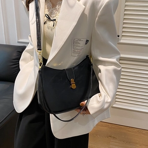 Minimalist black crescent shoulder bag with gold hardware worn with a white blazer