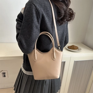 Minimalist beige bucket bag with round handles and long strap shown in a lifestyle setting