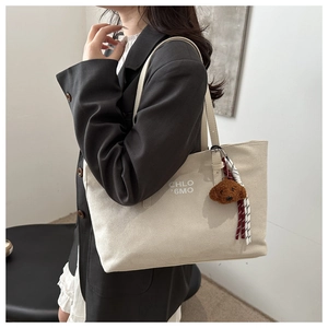 Detail view of cream canvas tote bag with brown bear charm and slim shoulder straps