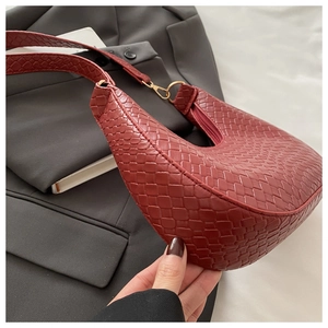 Détail du sac hobo tressé rouge brique avec anneau doré et fermeture éclair sur fond gris