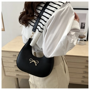 Detail of black leather half-moon shoulder bag with elegant gold bow metal buckle
