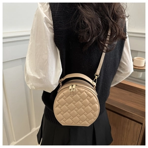 Close-up of a beige quilted round crossbody bag worn by a model in a minimalist room