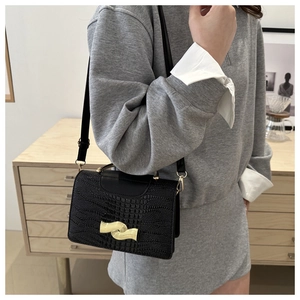 Detail of black crossbody bag with faux crocodile pattern and golden wavy metal clasp