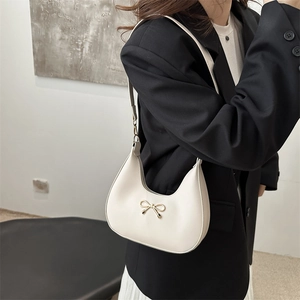 Chic white half-moon hobo bag with gold bow detail, worn with a classic black blazer