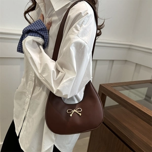 Dark brown crescent underarm bag with golden bow decoration on model in interior setting