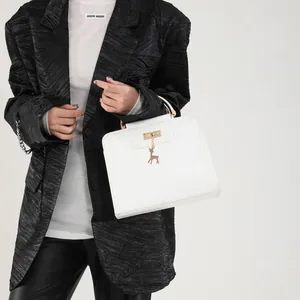 Chic white square handbag with golden deer charm and handle, styled with a black blazer