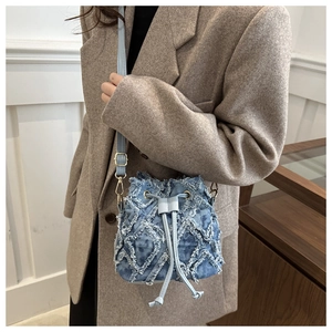 Detail of blue denim bucket bag with distressed diamond pattern and golden hardware