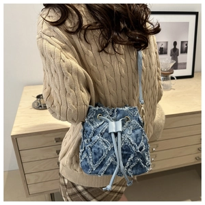Detail of blue denim patchwork bucket bag with frayed edges and drawstring closure