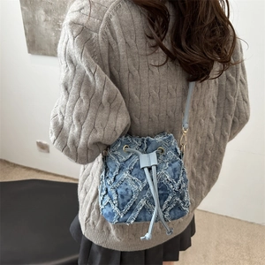 Blue denim bucket bag with frayed diamond stitching and chain strap on female model