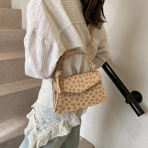 Detail of beige crossbody bag featuring clover embossed pattern and elegant knotted handle