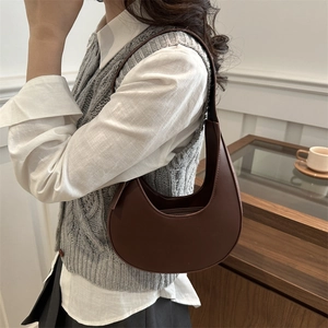Brown leather crescent shoulder bag styled with a minimalist outfit in a cozy cafe setting
