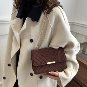 Close-up of deep brown chevron quilted faux suede chain bag on a beige coat