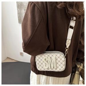 Detail view of beige monogram crossbody bag with SM logo and wide fabric strap on model