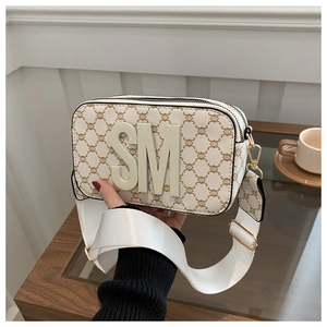 Close-up of beige square crossbody bag with vintage monogram and wide strap