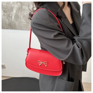 Detail of red leather bag showing the elegant golden bow clasp on the front flap