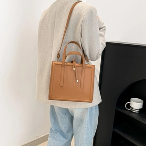 Minimalist caramel rectangle crossbody bag with dual handles shown on a blazer model