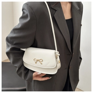 Detail of white leather shoulder bag with golden butterfly buckle worn on grey blazer