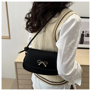 Detail showing a black leather shoulder bag with a gold bow buckle on a model