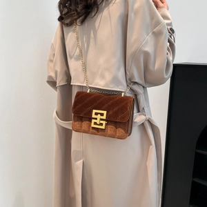 Brown velvet quilted chain bag for women with gold geometric buckle on a beige coat